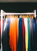 An array of colorful sweaters neatly hanging on a clothing rack. The garments are arranged in a spectrum of colors from dark shades to bright hues.