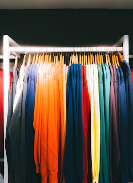 An array of colorful sweaters neatly hanging on a clothing rack. The garments are arranged in a spectrum of colors from dark shades to bright hues.