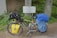 A touring bicycle is equipped with a variety of gear, including saddlebags and a handlebar bag. It is parked beside a multilingual sign indicating a watershed, surrounded by green vegetation and placed against a concrete structure.
