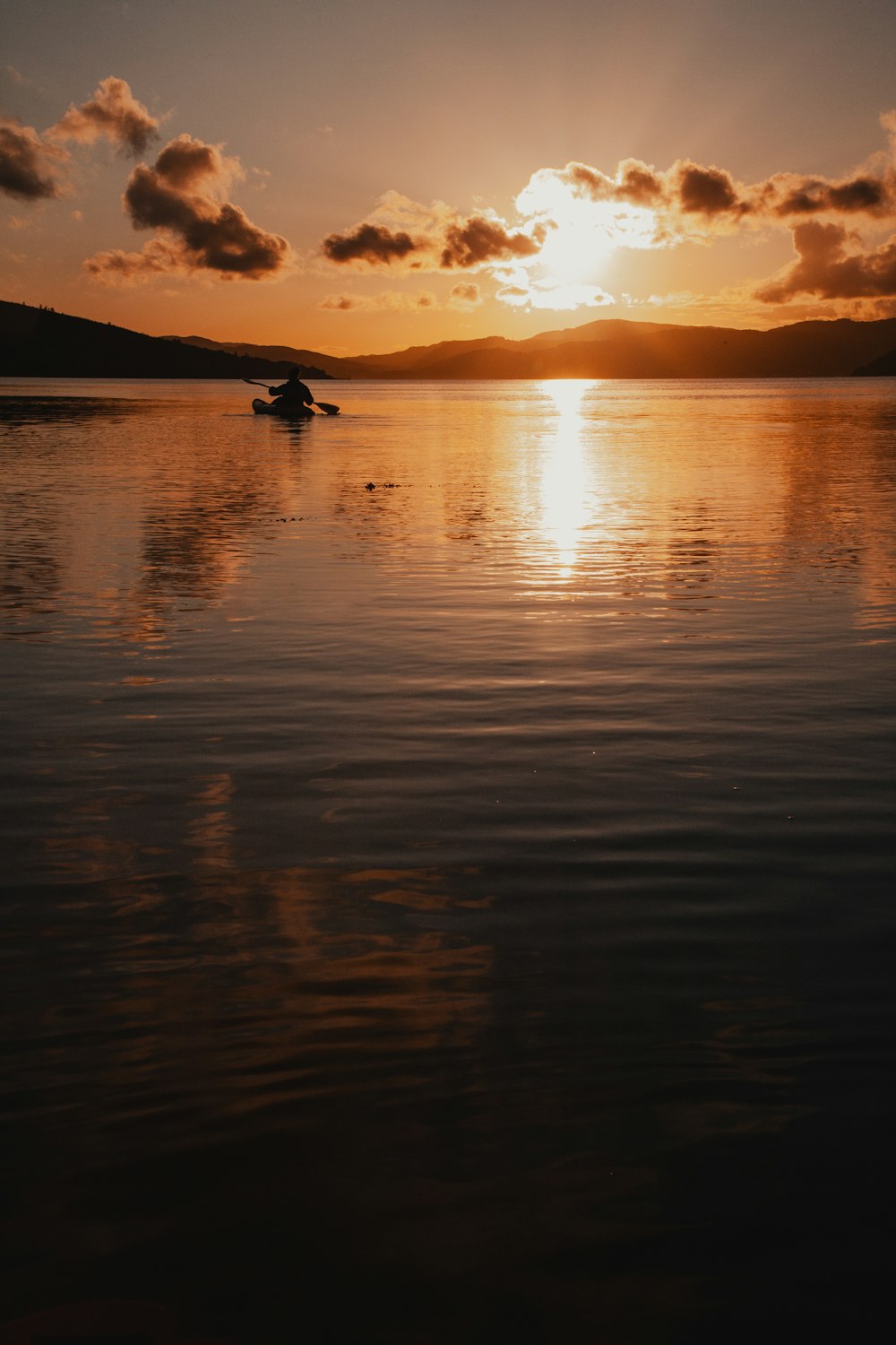 a person in a small boat on a lake at sunset