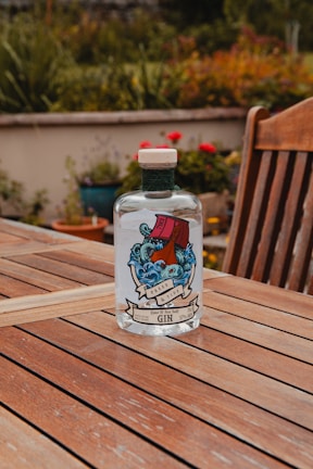 Elegant bottle of Roya Gin resting on a wooden table surrounded by blooming rose bushes at sunset.