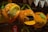 Plush toys shaped like pumpkins are displayed on a shelf. Two pumpkins have star and geometric shapes on them, while one is open to reveal a cat and another animal inside. Green fabric is used to represent the pumpkin stems.