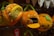 Plush toys shaped like pumpkins are displayed on a shelf. Two pumpkins have star and geometric shapes on them, while one is open to reveal a cat and another animal inside. Green fabric is used to represent the pumpkin stems.