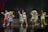 A group of performers in colorful animal costumes stand on a stage, each striking playful poses. The characters include a rabbit, a bear, a duck, and others, wearing vibrant outfits with various designs. The background appears to be a dark stage setting with subtle scenic elements.