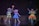 Three performers are on stage, dressed as vibrant characters. Two of them wear bear costumes with colorful outfits—one in yellow and another in blue, holding a bright staff. The third performer wears an elaborate fairy costume with a glowing orange and yellow dress, wings, and antennae. The background is dark, resembling a theater setting.