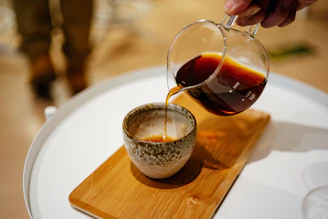 Close-up of hands pouring freshly brewed coffee into a ceramic cup.