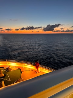 A joyful traveler standing on a cruise ship deck, looking at a glowing sunset over the ocean.