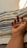 A hand is resting on a striped fabric surface, with fingers partially curled and displaying a reddish-brown stain on the fingertips. The fabric features horizontal stripes in shades of blue, beige, and white.