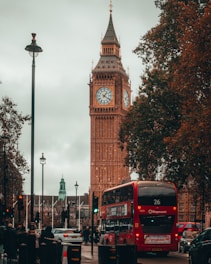 a red double decker bus driving past a tall clock tower