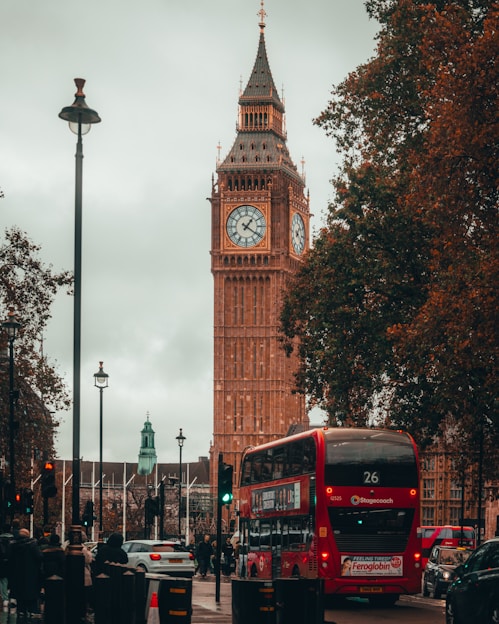 a red double decker bus driving past a tall clock tower