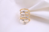 A gold ring with delicate floral designs encrusted with small diamonds, displayed on a soft white fabric background.
