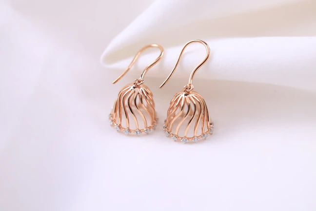 Close-up of elegant rose gold earrings with delicate floral design on a soft beige background.