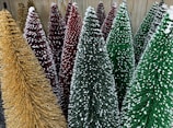 A collection of decorative Christmas trees with textured surfaces and snow-like accents. The trees vary in colors including gold, red, and green, and are densely packed together.