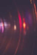 Abstract blurry lines in motion featuring a mixture of warm and cool colors, with prominent streaks of red, purple, and orange against a dark background.