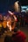 A performer is juggling with flaming torches in front of a crowd of spectators, including many children. The scene takes place outdoors, likely during a festival or public event at night. The audience is bundled up in winter clothing, suggesting cold weather.