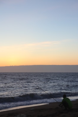 An angler casting a line into calm ocean waters at dawn.