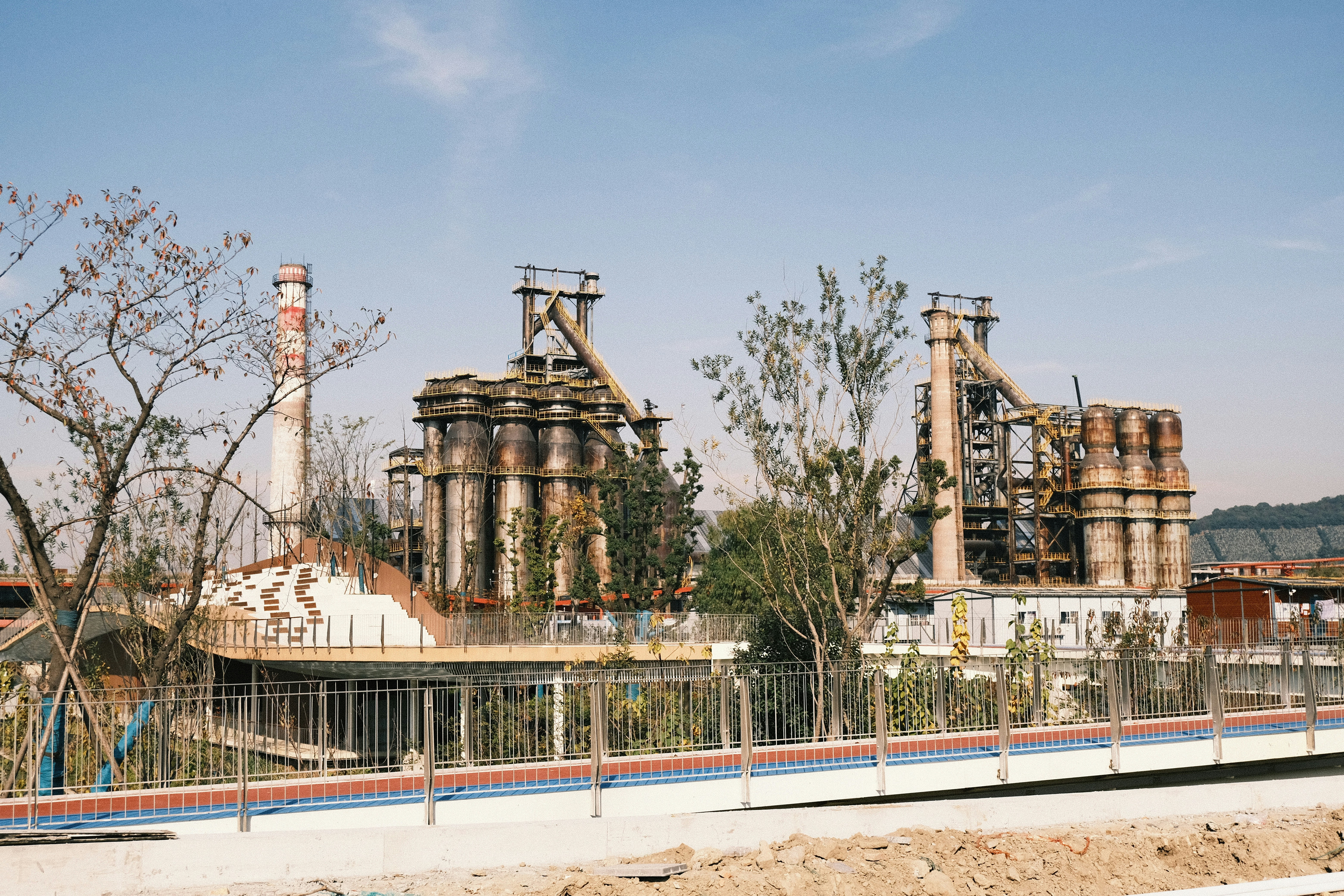 an abandoned factory with a fence and trees in the foreground