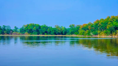 A tranquil lake reflecting autumn trees under a clear blue sky.