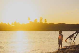A serene scene of a child sitting peacefully by a calm sea at sunset, surrounded by soft natural light.