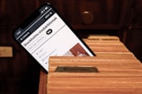 A smartphone screen displays a webpage for the Stockholm City Library, featuring a search bar and library-related options. The phone is placed inside a wooden card catalog drawer filled with organized index cards.