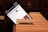 A smartphone screen displays a webpage for the Stockholm City Library, featuring a search bar and library-related options. The phone is placed inside a wooden card catalog drawer filled with organized index cards.