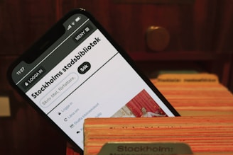 A smartphone displays the webpage of Stockholm's city library. It is placed within the slots of a wooden card catalog, suggesting a combination of modern and traditional library systems.
