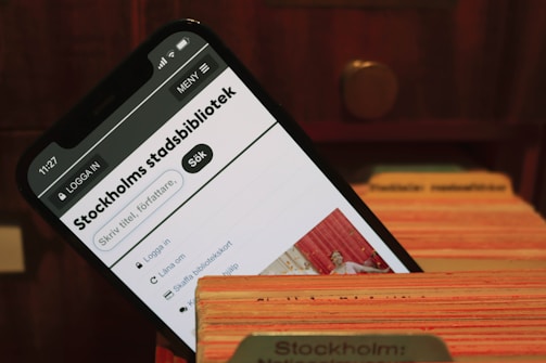 A smartphone displays the webpage of Stockholm's city library. It is placed within the slots of a wooden card catalog, suggesting a combination of modern and traditional library systems.
