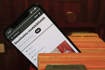 A smartphone displays the webpage of Stockholm's city library. It is placed within the slots of a wooden card catalog, suggesting a combination of modern and traditional library systems.