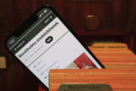 A smartphone displays the webpage of Stockholm's city library. It is placed within the slots of a wooden card catalog, suggesting a combination of modern and traditional library systems.