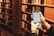 A person is holding a smartphone in a library setting. The phone screen displays information, likely from a library app or website, and bookshelves filled with books are visible in the background.