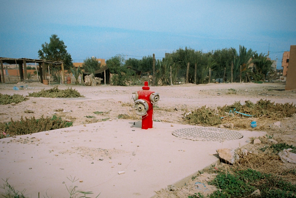 a red fire hydrant sitting in the middle of a dirt field