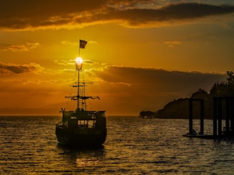 Sunset over the ocean with a silhouette of a ship sailing steadily on the horizon.