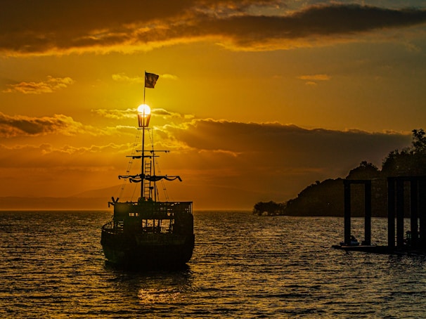 Sunset over the ocean with a silhouette of a ship sailing steadily on the horizon.