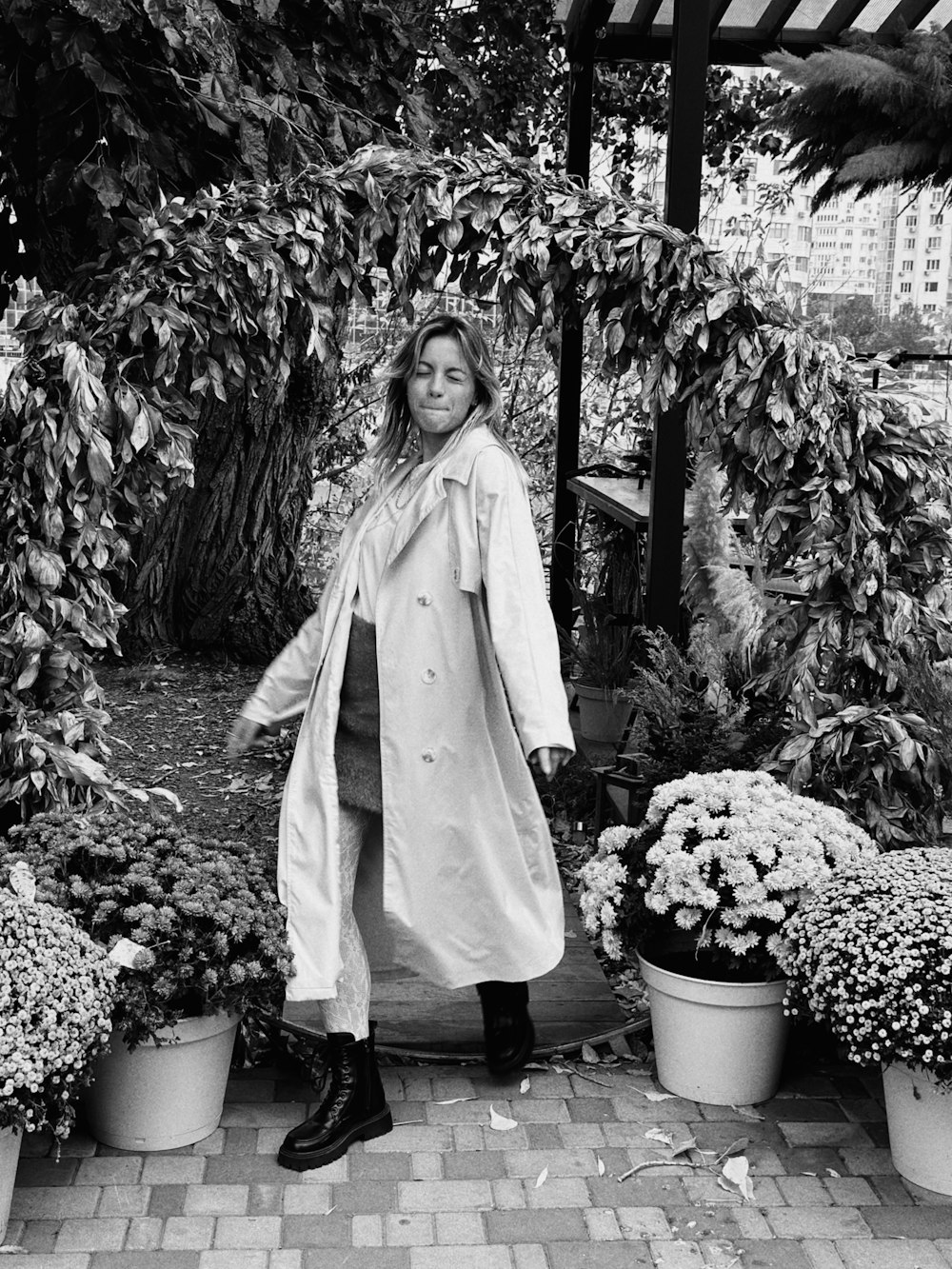 a woman in a trench coat standing in a garden