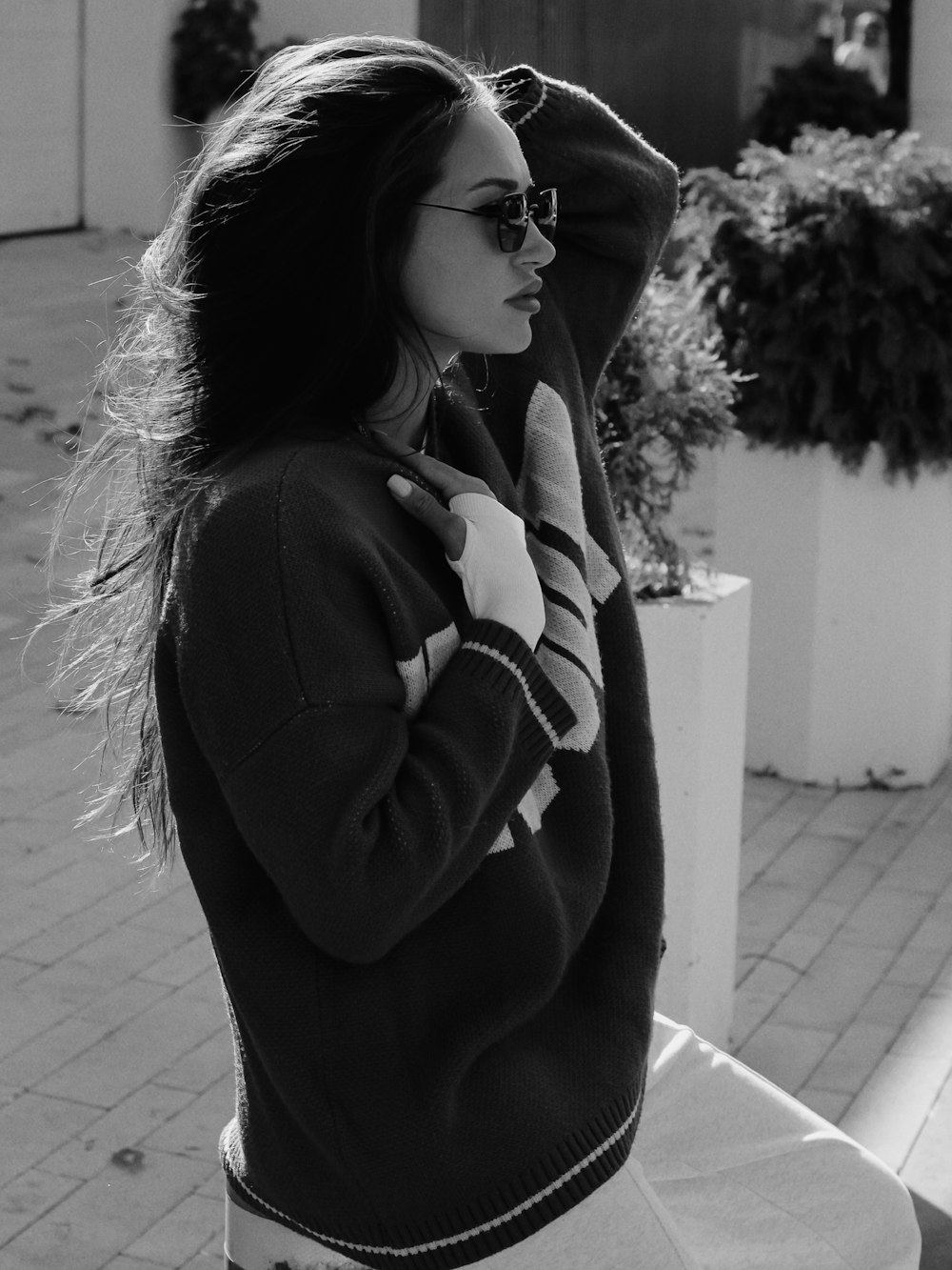 a woman in a sweater and sunglasses is standing on a sidewalk