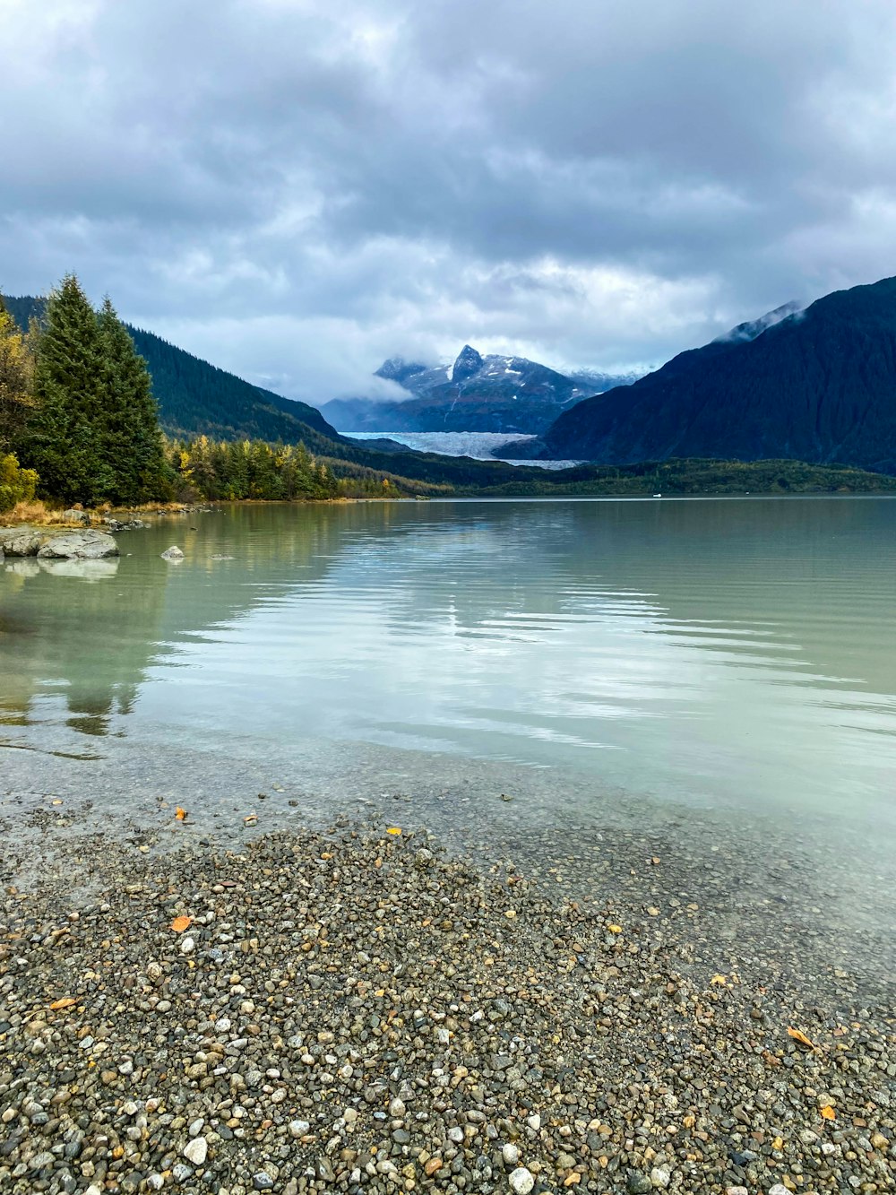 a body of water surrounded by mountains under a cloudy sky