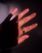 A hand model wearing a sleek silver signet ring set against a dark background with subtle lighting.
