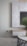 A modern living room corner featuring a sleek, light gray textured wall with a mounted cabinet and a large flat-screen television. In the foreground, a round marble-topped coffee table with a black metal base is partially visible. A large vase with green foliage is placed on the table, adding a touch of nature to the space. The room has a minimalist design with soft neutral tones.