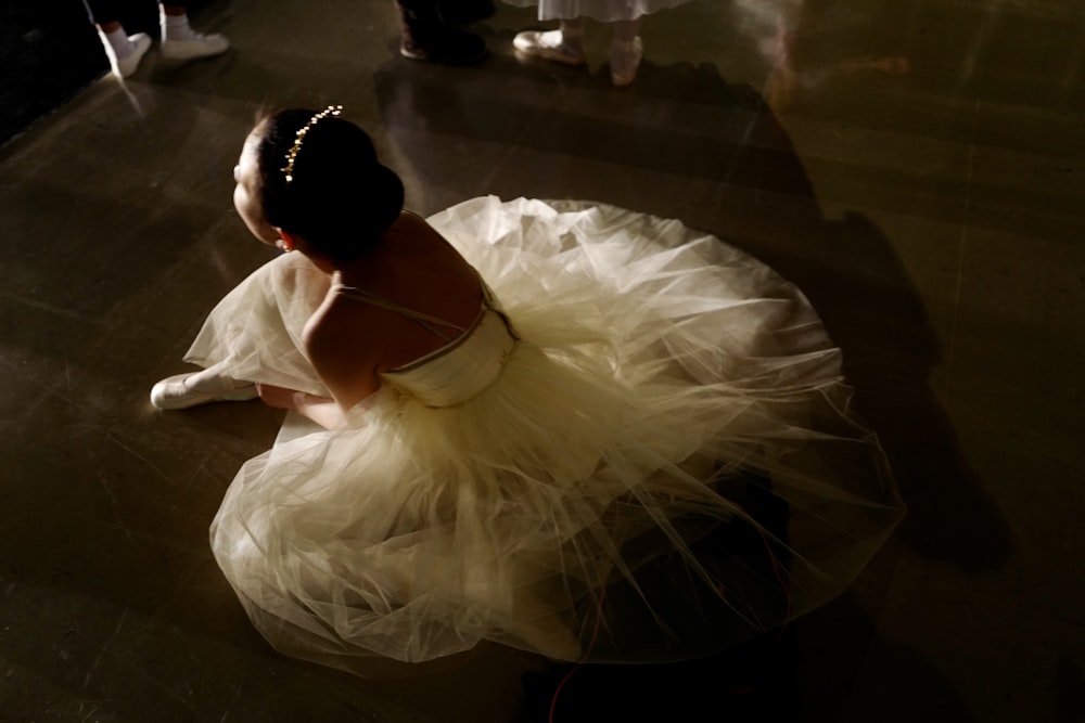 a little girl in a white dress sitting on the floor