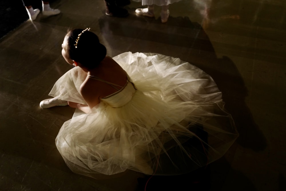 una niña con un vestido blanco sentada en el suelo