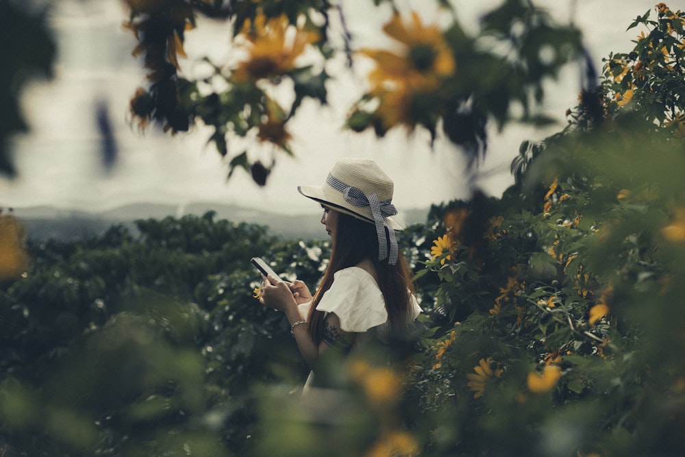 a woman standing in a field of sunflowers looking at her cell phone