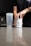 A person is opening a container labeled 'BUCKED UP' on a kitchen counter. Next to it is a transparent shaker bottle. The scene suggests a focus on fitness or supplementation.