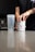 A person is opening a container labeled 'BUCKED UP' on a kitchen counter. Next to it is a transparent shaker bottle. The scene suggests a focus on fitness or supplementation.