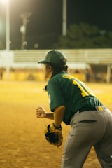 Action shot of a softball player in blue catching a fast pitch under bright stadium lights.