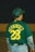 A person wearing a green baseball jersey with the number 28 and the name 'HERNANDEZ' on the back. The individual also wears a matching green baseball cap and grey pants with layered grey sleeves.