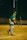 A baseball player in a green and yellow uniform stands on the pitcher's mound, preparing to throw a ball. Another player in the outfield is seen ready to catch. The game takes place on an illuminated field at night.