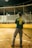 A baseball player stands on a field, holding a bat. The player is wearing a green jersey with the name 'CASTAÑEDA' and number '8' on the back. The field is lined with a yellow barrier, and there are empty bleachers in the background under a partially covered roof. The scene appears to be at night, with artificial lighting illuminating the area.