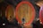Large wooden barrels with red rims are lined up in a dimly lit wine cellar with a brick ceiling. Each barrel has a spigot at the bottom for dispensing liquid.