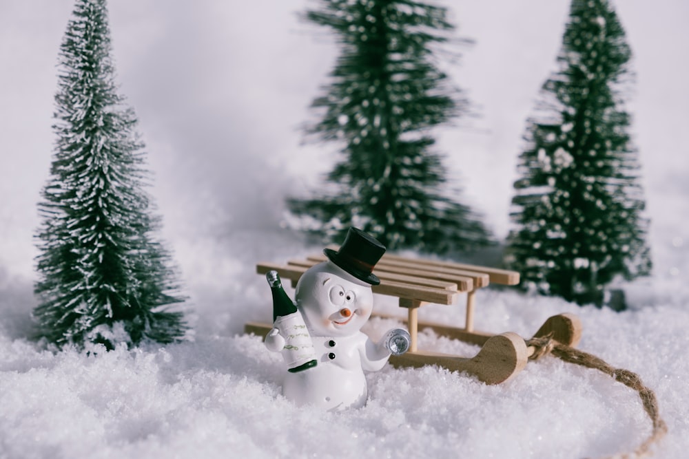 a snowman in the snow with a sleigh and trees in the background