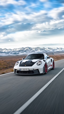 A luxury sports car gliding along an empty mountain highway under clear skies.